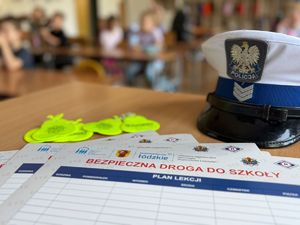 Na stole leżą czapka policyjna oraz materiały promocyjne akcji &quot;Bezpieczna droga do szkoły&quot;.