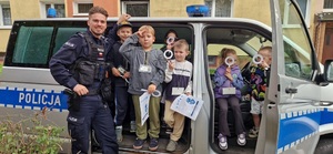 Wspólne zdjęcie umundurowanego policjanta oraz dzieci w radiowozie.