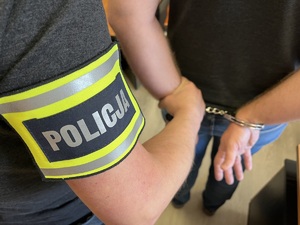 Zdjęcie poglądowe - policjant trzyma mężczyznę, który ma kajdanki założone na ręce z tyłu.