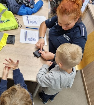 Policjantka pokazuje chłopczykowi jak pobiera się odciski palców.