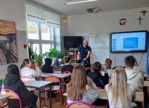 Umundurowany Policjant, w klasie, w trakcie rozmowy z młodzieżą.