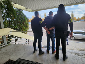 Policjanci trzymają mężczyznę, który ma kajdanki założone na ręce z tyłu.