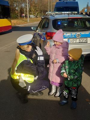 Policjantka przybija piętki z dziećmi, które noszą elementy odblaskowe.