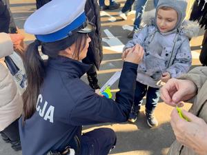 Policjantka daje element odblaskowy dziecku.