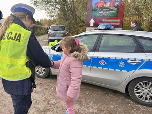 Policjantka przekazuje element odblaskowy dziewczynce.