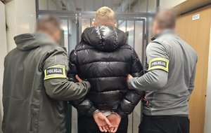 Policjanci trzymają mężczyznę, który ma kajdanki założone na ręce z tyłu.