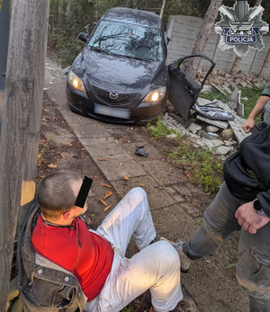 Zatrzymany przez policjantów mężczyzna, w tle rozbite auto.