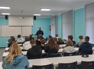 Policjant, w klasie, podczas zajęć z młodzieżą.