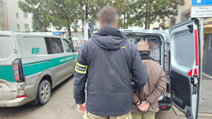 Policjant stoi z zatrzymanym mężczyzną przed radiowozem.