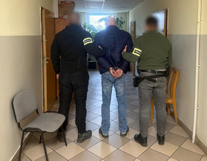 Policjanci trzymają mężczyznę, który ma założone kajdanki na ręce z tyłu.