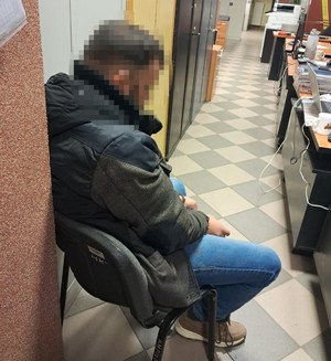 Mężczyzna z kajdankami założonymi na ręce z przodu siedzi na krześle.