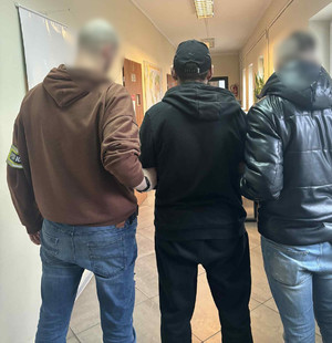 Policjanci stoją z zatrzymanym mężczyzną.