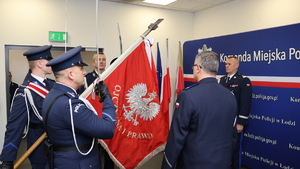 Policjanci stoją przy sztandarze Komendy Miejskiej Policji w Łodzi.