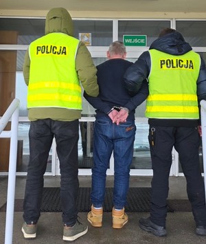 Policjanci trzymają mężczyznę, który ma założone kajdanki na ręce z tyłu.