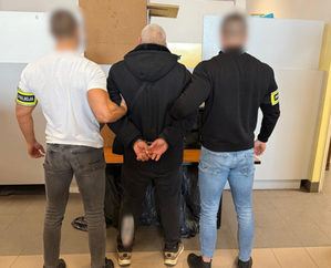 Policjanci trzymają mężczyznę, który ma założone kajdanki na ręce z tyłu.