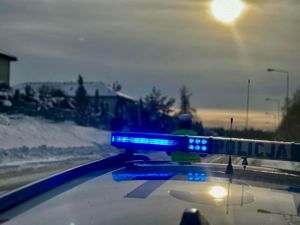Belka z sygnałami świetlnymi na dachu radiowozu, przed pojazdem stoi policjant Wydziału Ruchu Drogowego.