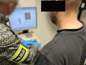 Policjant pobiera odciski palców od zatrzymanego.