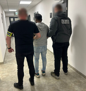 Policjant i funkcjonariusz Straży Granicznej z zatrzymanym obcokrajowcem.