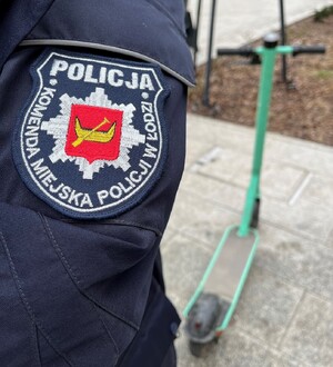 Zdjęcie poglądowe - naszywka Komendy Miejskiej Policji w Łodzi na rękawie munduru, a w tle stoi hulajnoga elektryczna.