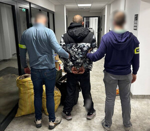 Policjanci trzymają mężczyznę, który ma założone kajdanki na ręce z tyłu.