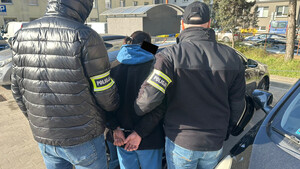 Policjanci prowadzą mężczyznę, który ma założone kajdanki na ręce z tyłu .