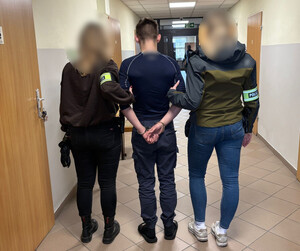 Policjantki trzymają mężczyznę, który ma założone kajdanki na ręce z tyłu.