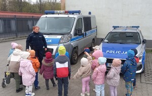 Policjantka i przedszkolaki przed oznakowanymi radiowozami policyjnymi.