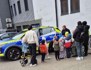 Policjantka prezentuje przedszkolakom oznakowany radiowóz policyjny.