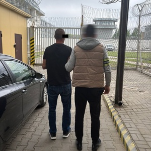 Policjant prowadzi zatrzymanego mężczyznę.