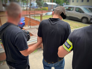 Policjanci trzymają mężczyznę, który ma założone kajdanki zespolone.
