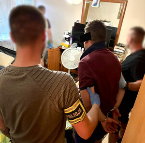 Policjanci trzymają mężczyznę, który ma założone kajdanki na ręce z tyłu.