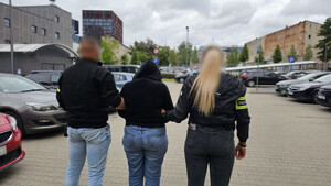 Policjanci prowadzą zatrzymaną kobietę.