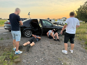 Policjanci pilnują zatrzymanych mężczyzn przy pojeździe.
