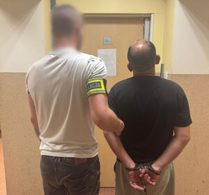 Policjant trzyma mężczyznę, który ma założone kajdanki na ręce z tyłu.