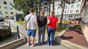 Policjanci trzymają zatrzymanego mężczyznę.