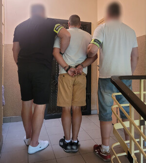 Policjanci trzymają mężczyznę, który ma założone kajdanki na ręce z tyłu.