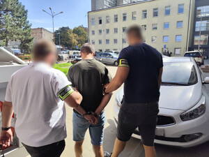 Policjanci prowadzą mężczyznę, który ma założone kajdanki na ręce z tyłu.
