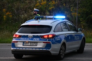 Radiowóz policyjny oraz policjant na drodze.