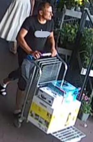 Mężczyzna w wieku około 40 lat szczupłej budowy ciała. Ubrany był w  ciemną koszulkę typu T-shirt z jasnym napisem, ciemne spodenki za kolano, ciemne klapki i białe skarpetki.
