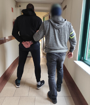 Policjant prowadzi zatrzymanego mężczyznę.