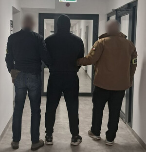 Policjanci prowadzą zatrzymanego mężczyznę.