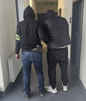 Policjant z zatrzymanym mężczyzną na korytarzu.