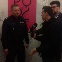 Komendant Miejski Policji insp. Paweł Karolak podczas udzielania wywiadu dwóm dziennikarzom na tle banera miasta Łodzi.