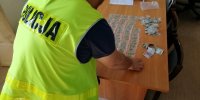 policjant z kamizelce odblaskowej z napisem policja pochylo9ny nad dilerkami z narkotykiem