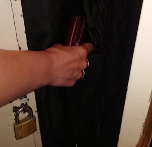 Na zdjęciu widoczna jest metalowa szafka na której założona jest kłódka. Obok widoczna jest otwarta szafka z wiszącą wewnątrz kurtką. Widać rękę, która wyjmuje portfel z kieszeni kurtki