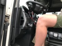 Na zdjęciu widzimy nogę kierowcy w ciężarówce. Widać na nim również podpięte urządzenie typu tachograf, które znajduje się poniżej kierownicy.