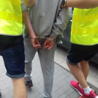 Na zdjęciu policjanci prowadzący zatrzymanego. W kadrze widać ręce mężczyzny skutego kajdankami.